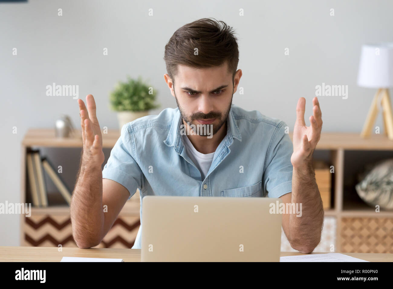 Irritated man looking at laptop screen sitting at the desk Stock Photo