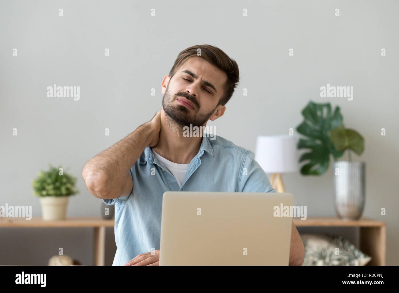 Tired man sitting at the desk has a neck pain Stock Photo