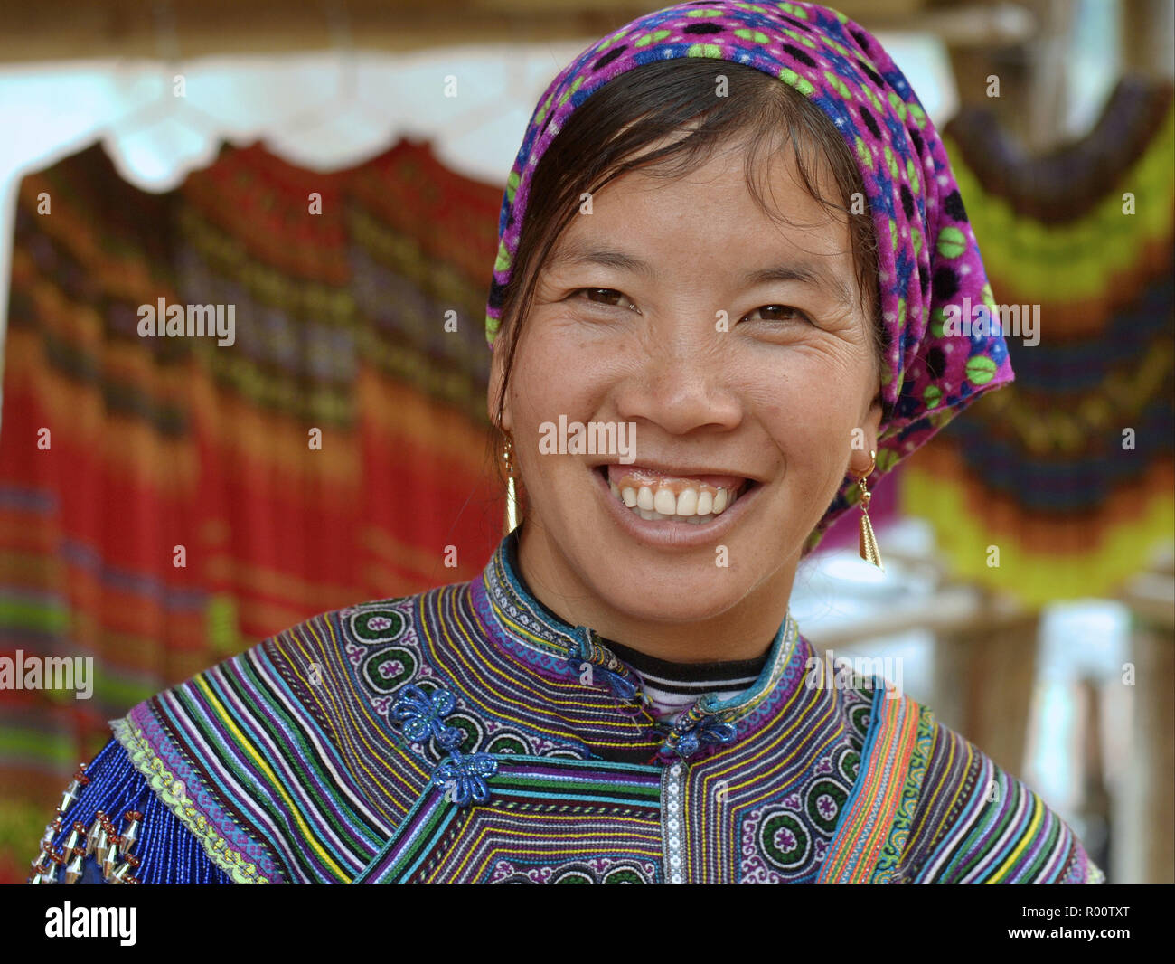 Young Vietnamese Flower H’mong hill-tribe woman wears embroidered Flower H’mong attire in blue and smiles for the camera. Stock Photo