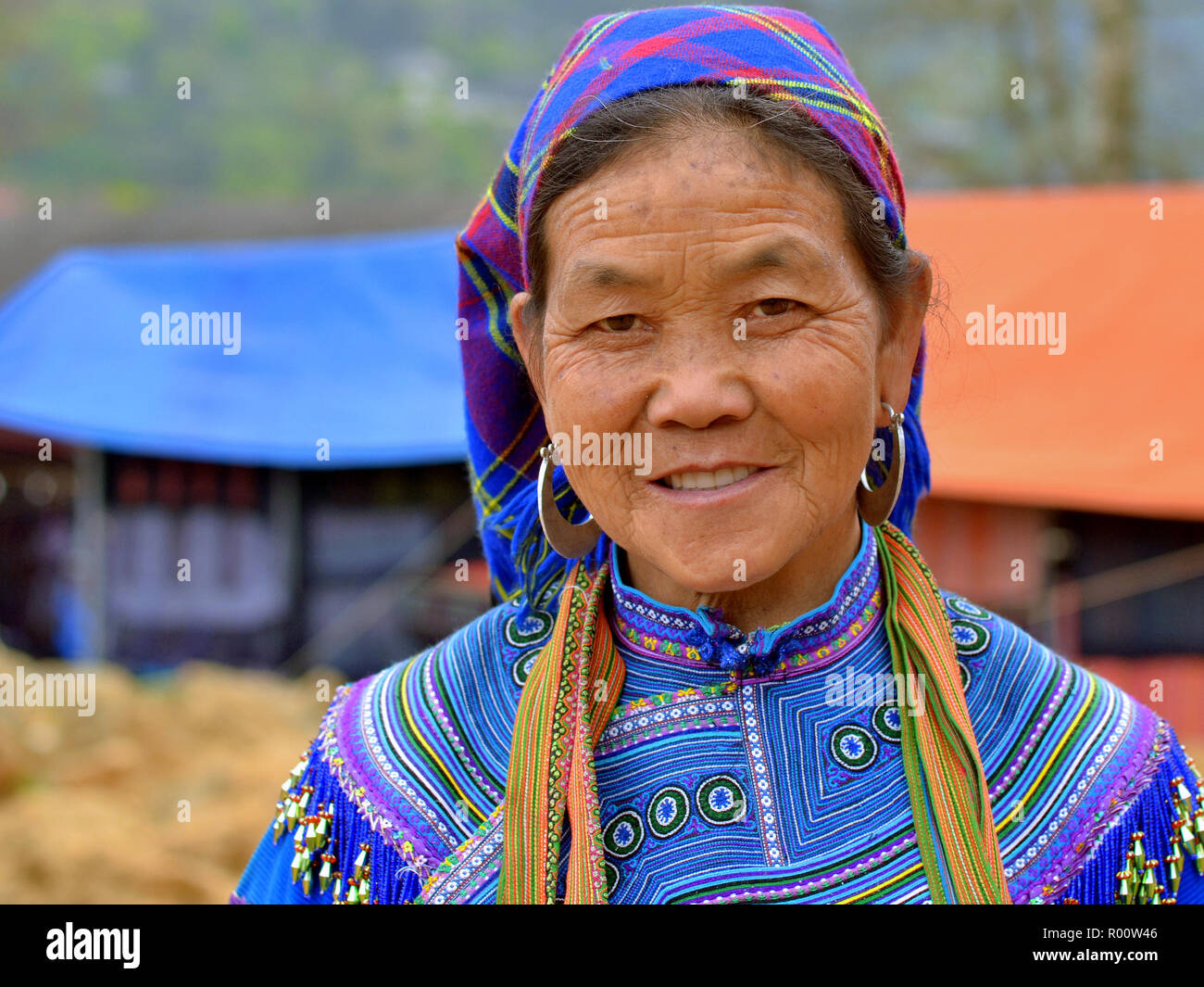 Elderly Vietnamese Blue H’mong woman with heavy silver earrings wears embroidered traditional H’mong attire in blue. Stock Photo