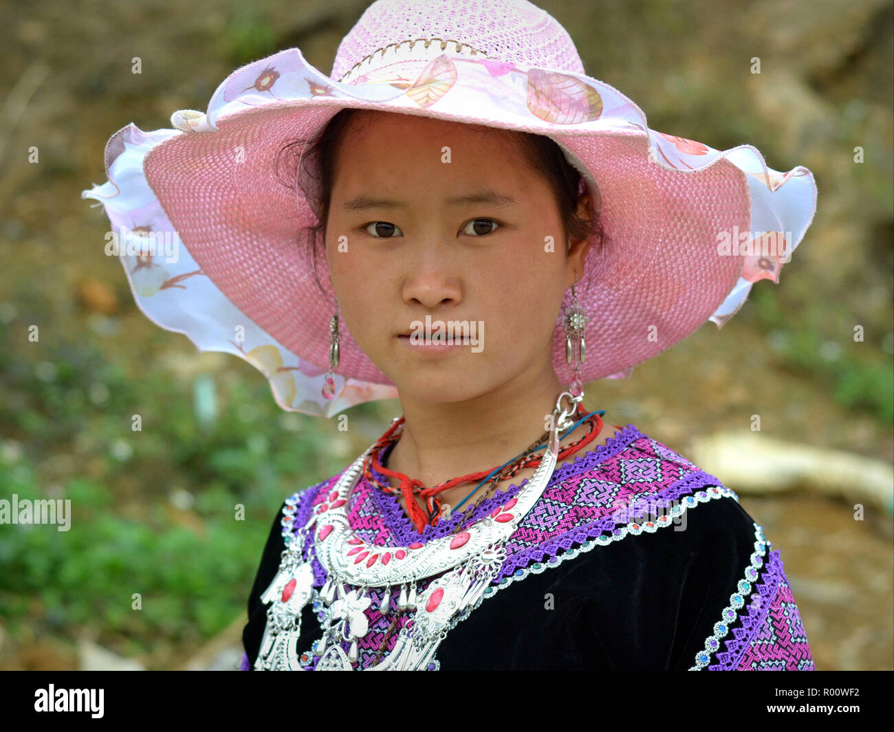 Vietnamese H’mong teenage girl wears an elegant sun hat in pink and tribal H’mong clothing with a heavy silver necklace. Stock Photo