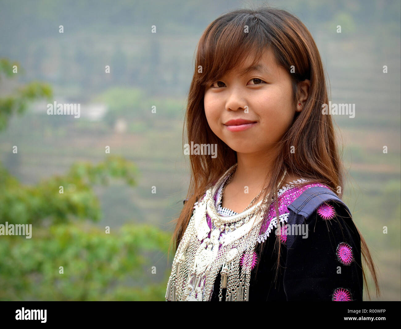 Pretty Vietnamese H’mong teenage girl wears her clan’s traditional outfit: embroidered black H’mong blouse with silver tribal necklace. Stock Photo