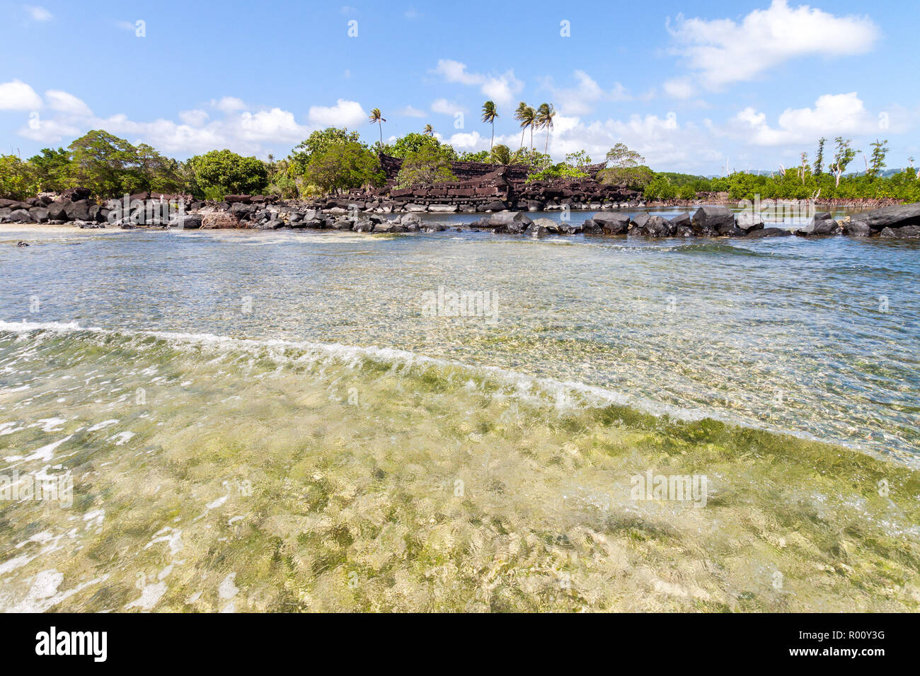 Wave in coral and sand shallow lagoon of Pohnpei, Micronesia, Oceania with overgrown Nan Madol prehistoric ruined in the background. Stock Photo