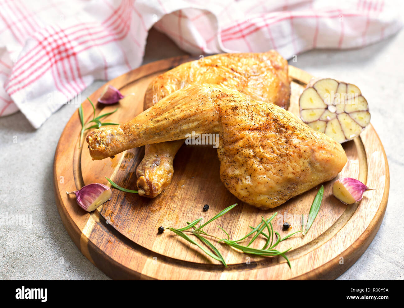 Delicious roast chicken leg or chicken drumsticks on a wooden cutting board. High angle view and fresh rosemary and garlic. Closeup shot, top view. Stock Photo