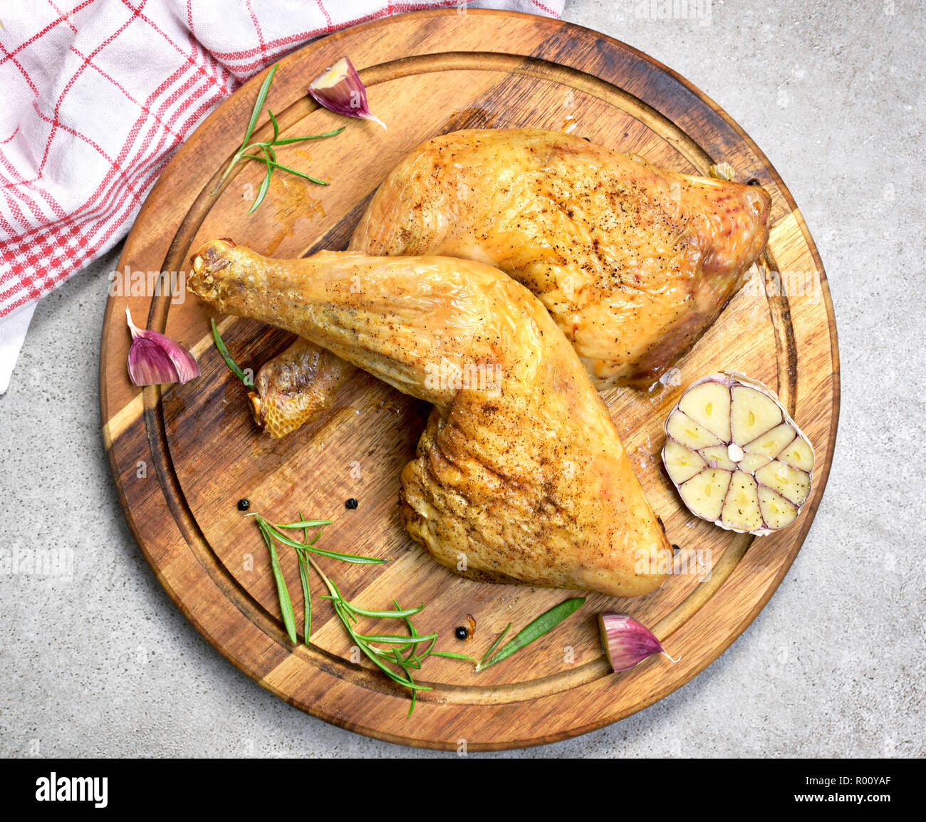 Delicious roast chicken leg or chicken drumsticks on a wooden cutting board. High angle view and fresh rosemary and garlic. Closeup shot, top view. Stock Photo