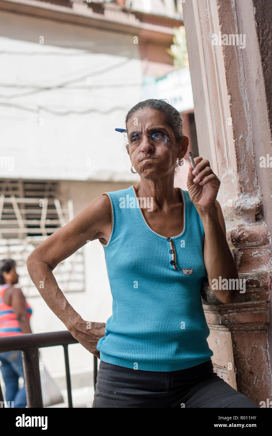A woman smokes a cigarette outside on a hot, sunny day in Havana, Cuba. Stock Photo