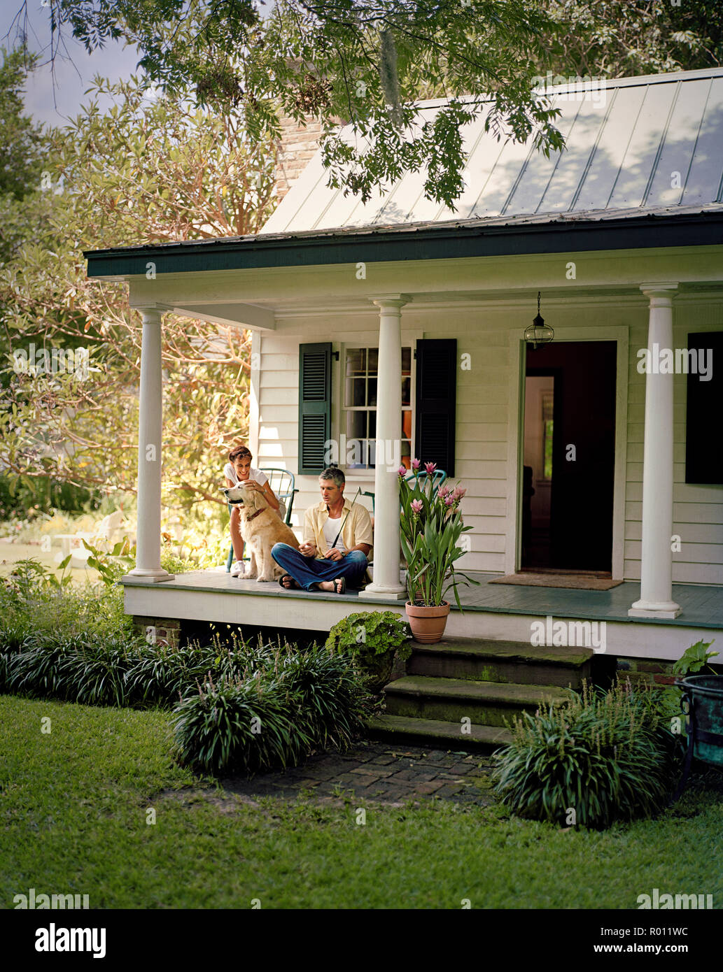 Mid-adult husband and wife sitting on a porch with their dog. Stock Photo