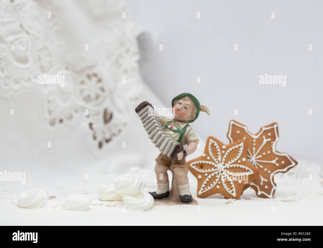 Porcelain boy figurine playing accordions in christmas interior with gingerbread stars and meringue rings Stock Photo