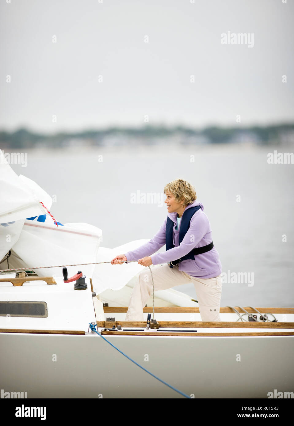 Mature adult woman winching a sail while on a boat. Stock Photo