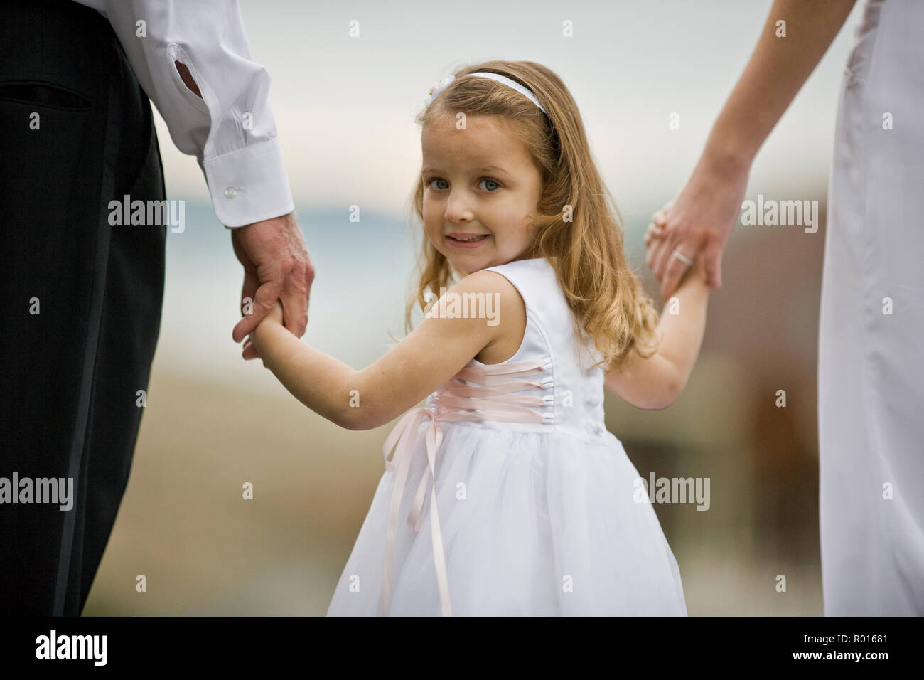 portrait of a young girl holding hands with a bride and groom while dressed as a flower girl. Stock Photo