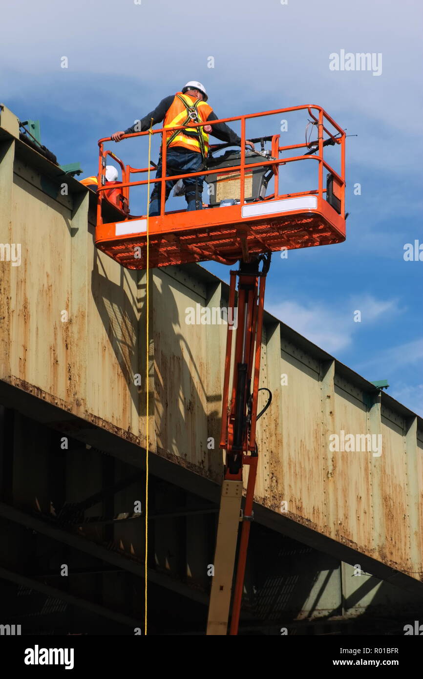 Infrastructure maintenance worker with safety harness working on a city elevated rail system in a boom lift or cherry picker. Stock Photo