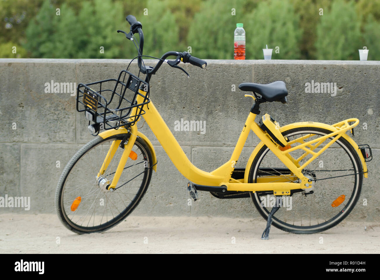 Yellow bike from bike sharing company parked next to the wall with drink and plastic cups Stock Photo