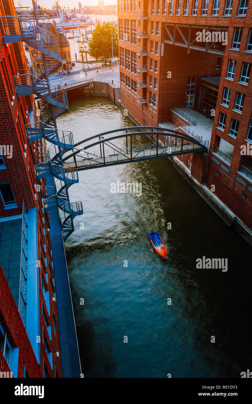 Small Boat under bridge over canal between red brick buildings in the old warehouse district Speicherstadt in Hamburg in golden hour sunset light, Germany. View from above Stock Photo