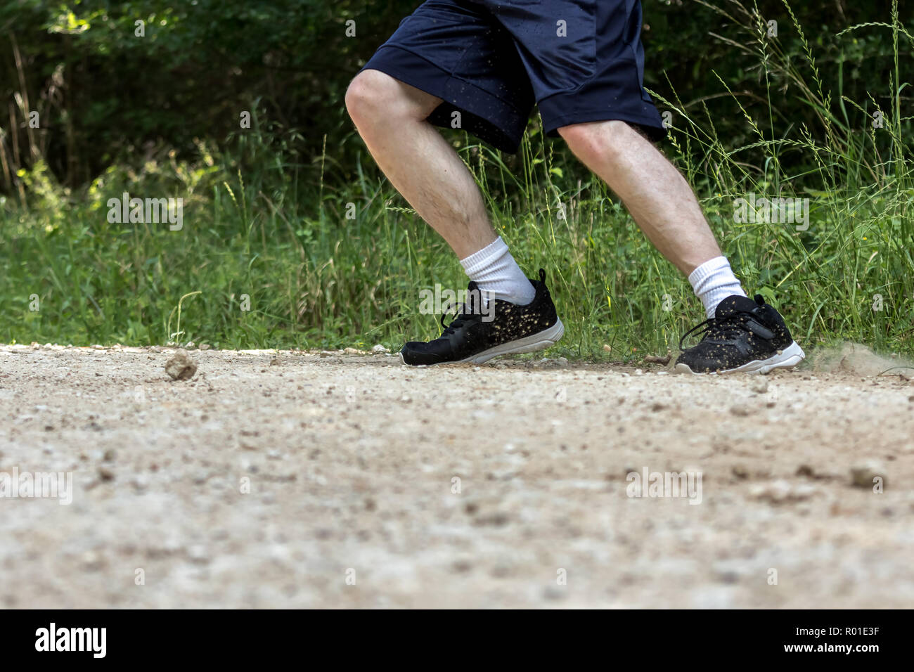 A man runs on a dirt path and kicks up dirt and rocks with his shoes. Stock Photo