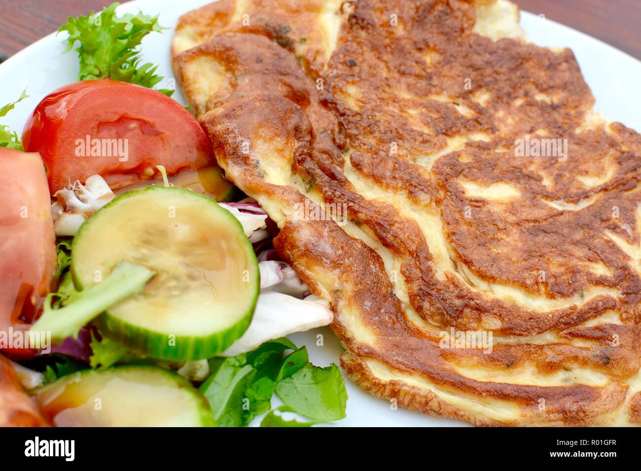 Golden cooked omelette with side salad served on a white plate Stock Photo