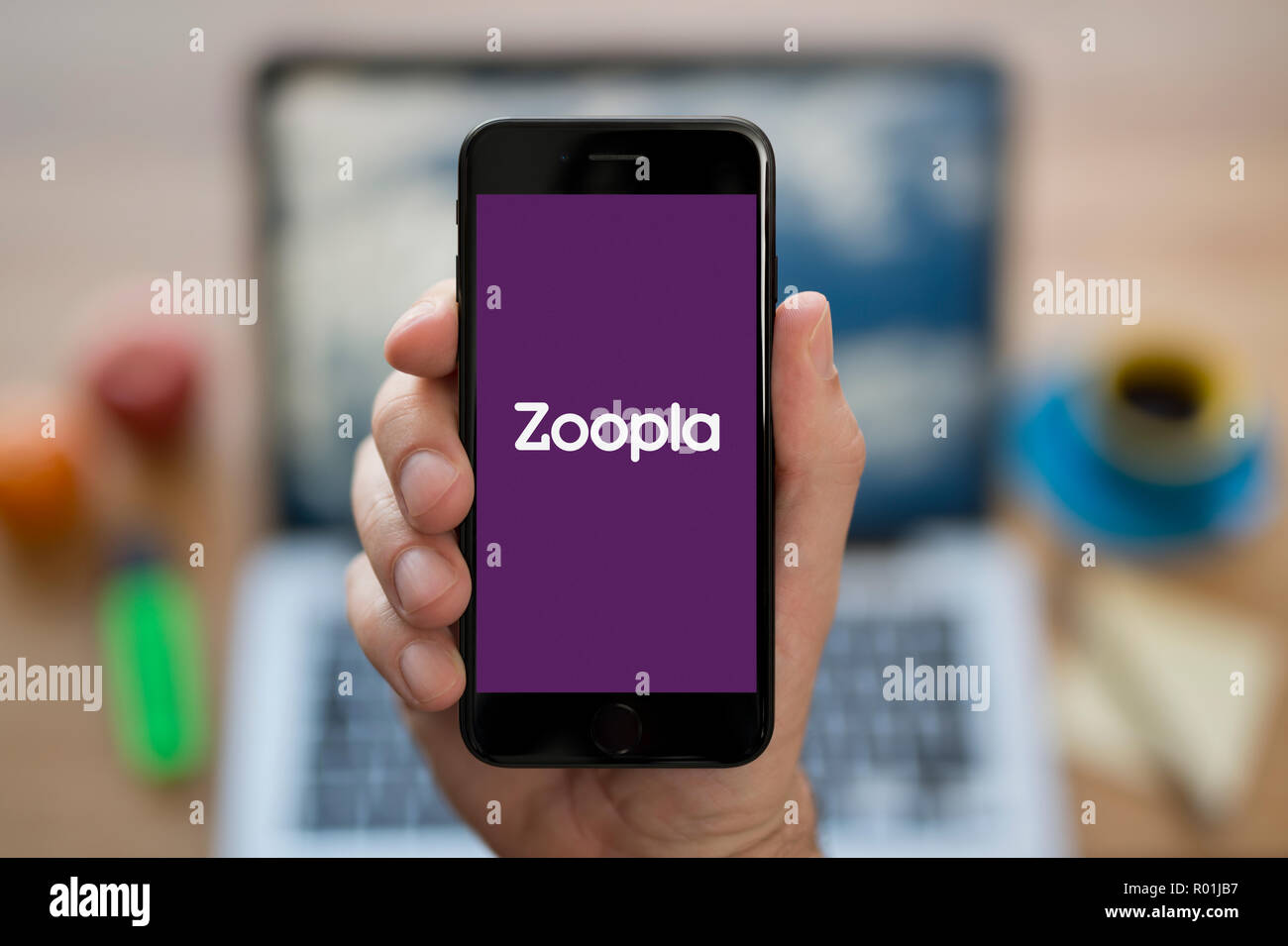 A man looks at his iPhone which displays the Zoopla logo, while sat at