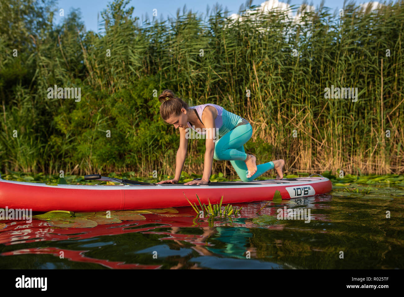 Photo of young woman doing hand stand on stand up paddle board. She