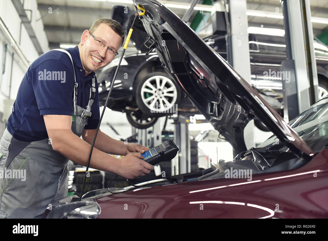 smiling car mechanic in a workshop - engine repair and diagnosis on a vehicle Stock Photo