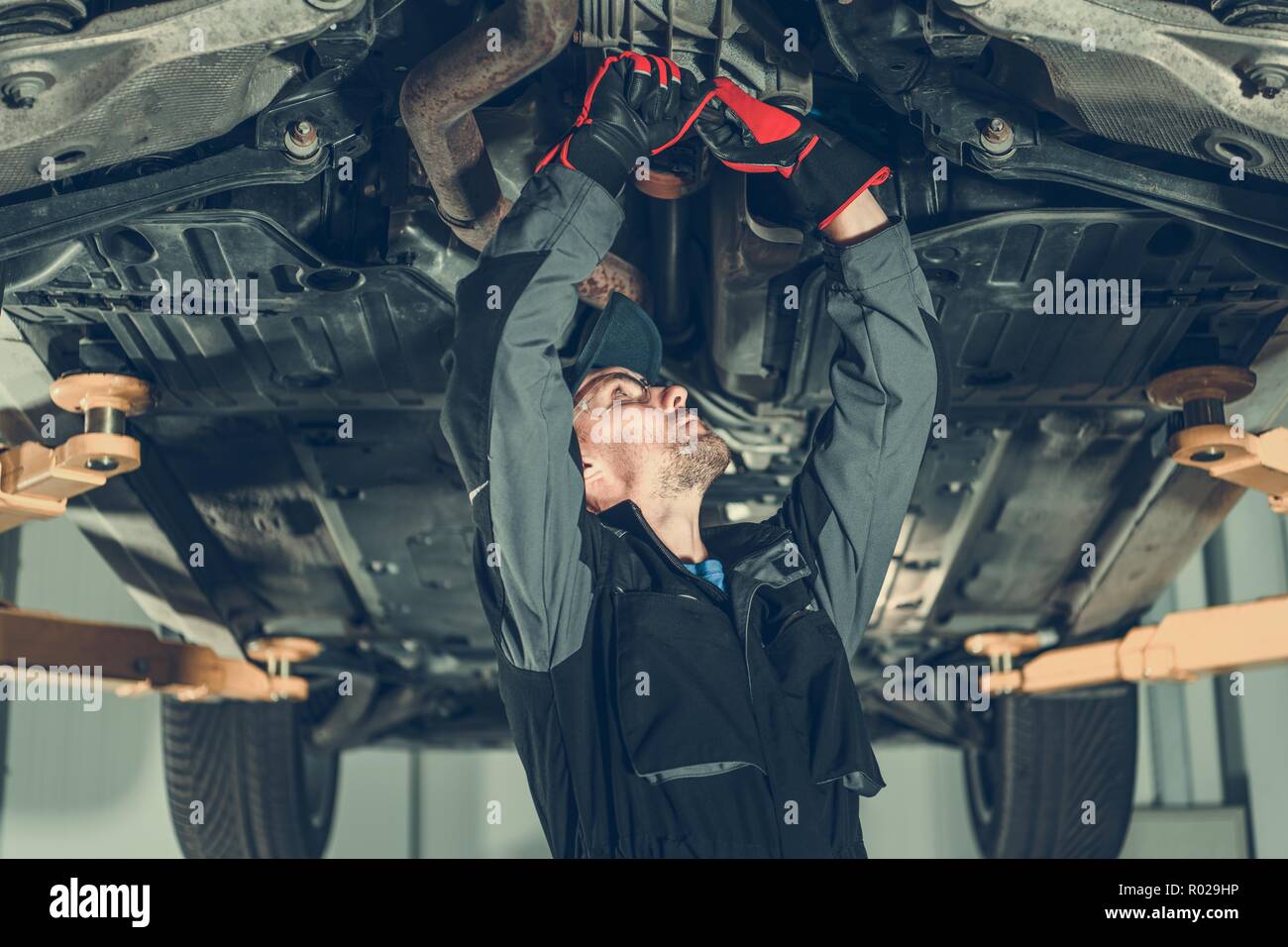 Car Mechanic Undercarriage Maintenance. Caucasian Worker Adjusting Tension on a Vehicle Drivetrain Elements. Stock Photo