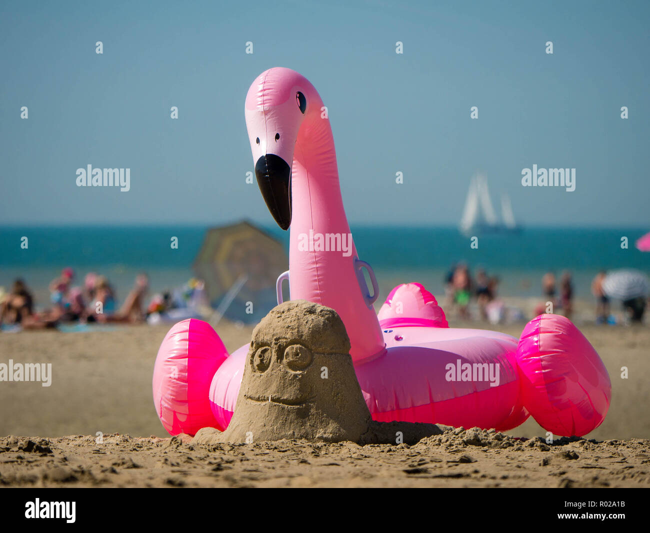 Beach scene during holidays with a sand minion and a inflatable Flamingo in the foreground Stock Photo