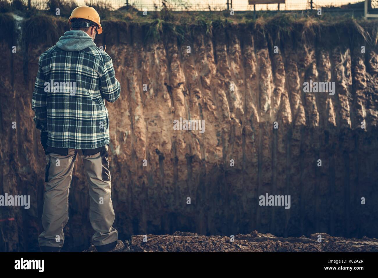 Ground Works Supervisor in Yellow Hard Hat Calling Other Worker Using Walkie Talkie. Construction Site Supervising. Stock Photo