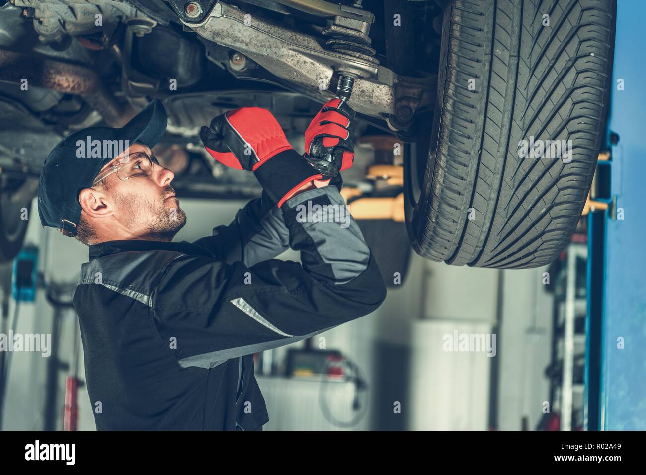 Caucasian Car Mechanic Adjusting Tension in Vehicle Suspension Element. Professional Automotive Service. Stock Photo