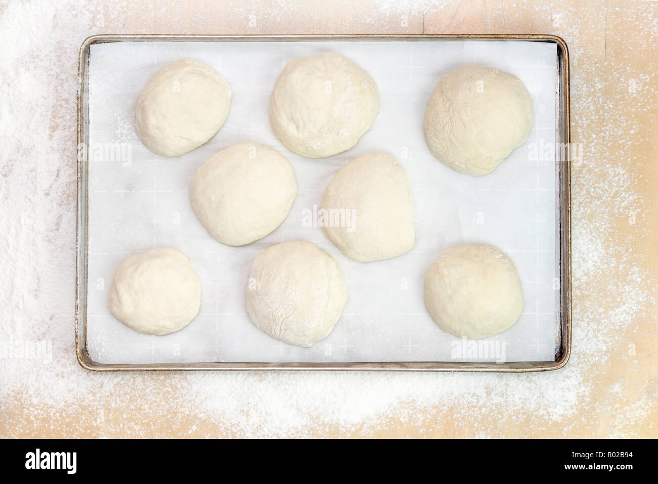 Balls of dough on parchment paper, on a metal tray on a wooden table covered with white flour. View from above. Stock Photo