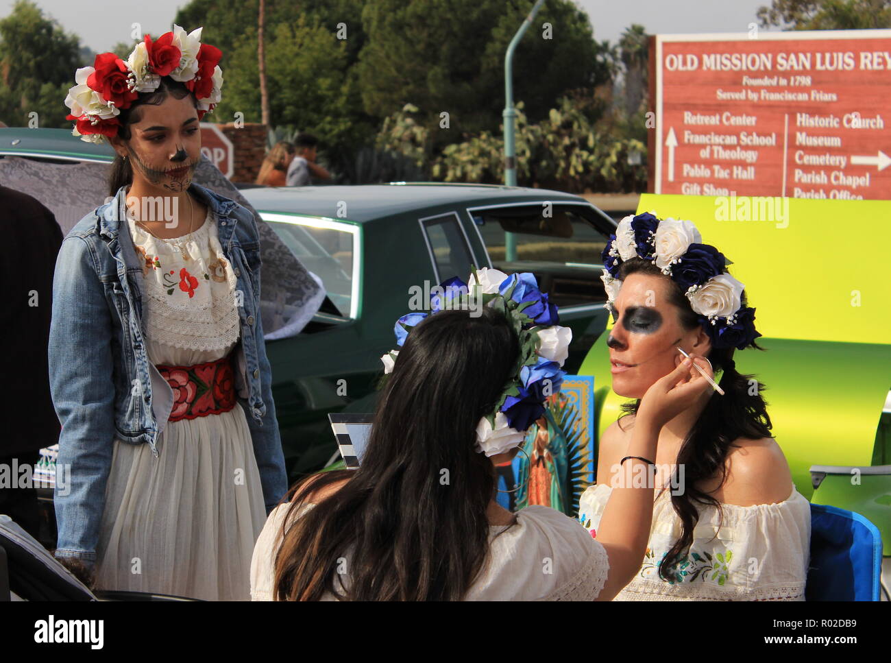 Three young woman putting on sugar skull (Catrina) makeup for Day of the Dead celebration Stock Photo