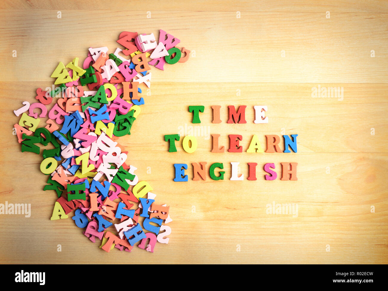 TIME TO LEARN ENGLISH wooden letters near a pile of other letters over wood board background Stock Photo