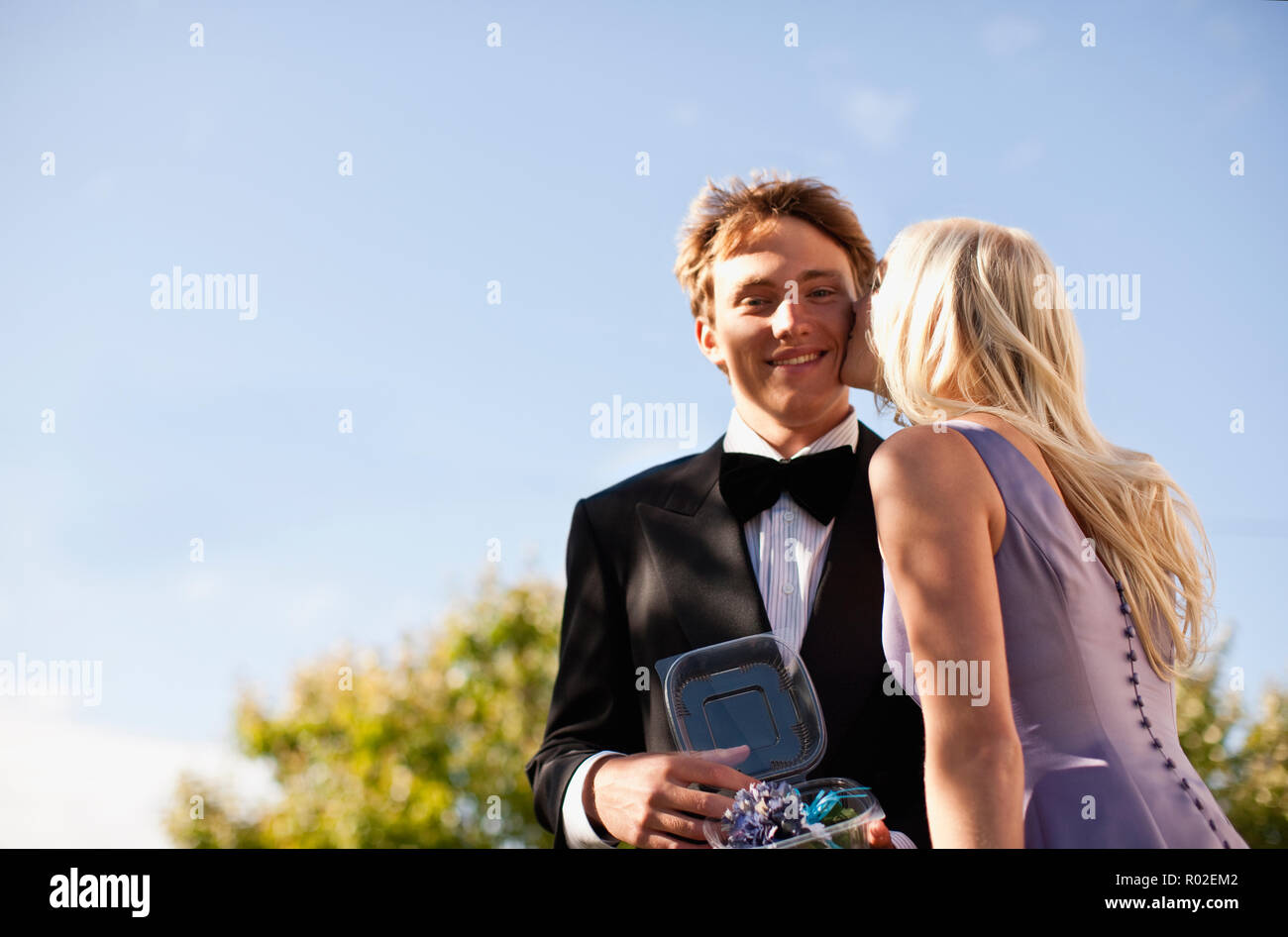 Teenage boy holding corsage in container as his prom date kisses his cheek. Stock Photo