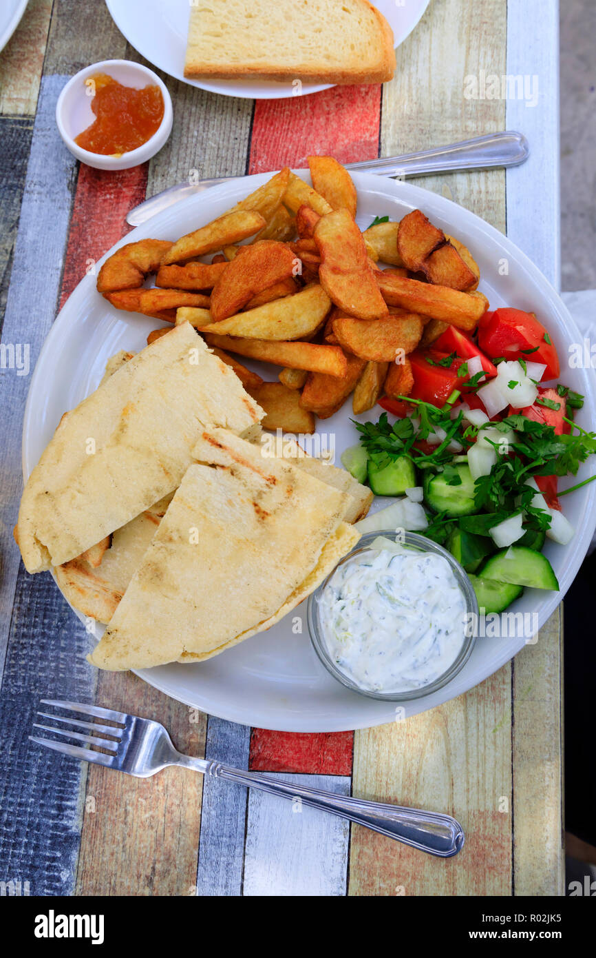 Cypriot food on a white plate at a village taverna. Halloumi in pitta bread, chips, salad and tzatziki , with a side order of toast and jam.Cyprus Oct Stock Photo