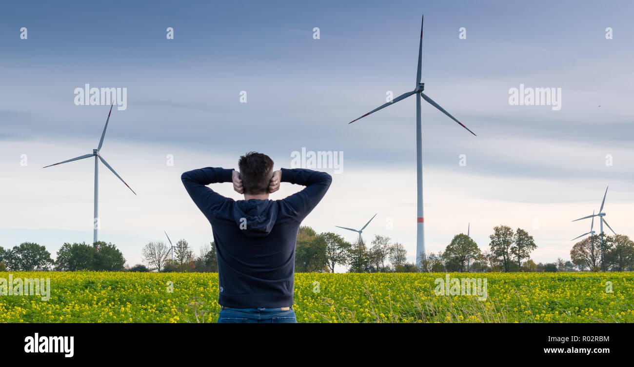 Man infront of a wind farm blocks his ears to reduce the noise Stock Photo