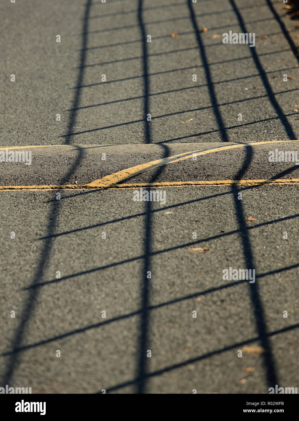 Shadow from a roadside fence cast over a speed hump on the road surface. Stock Photo
