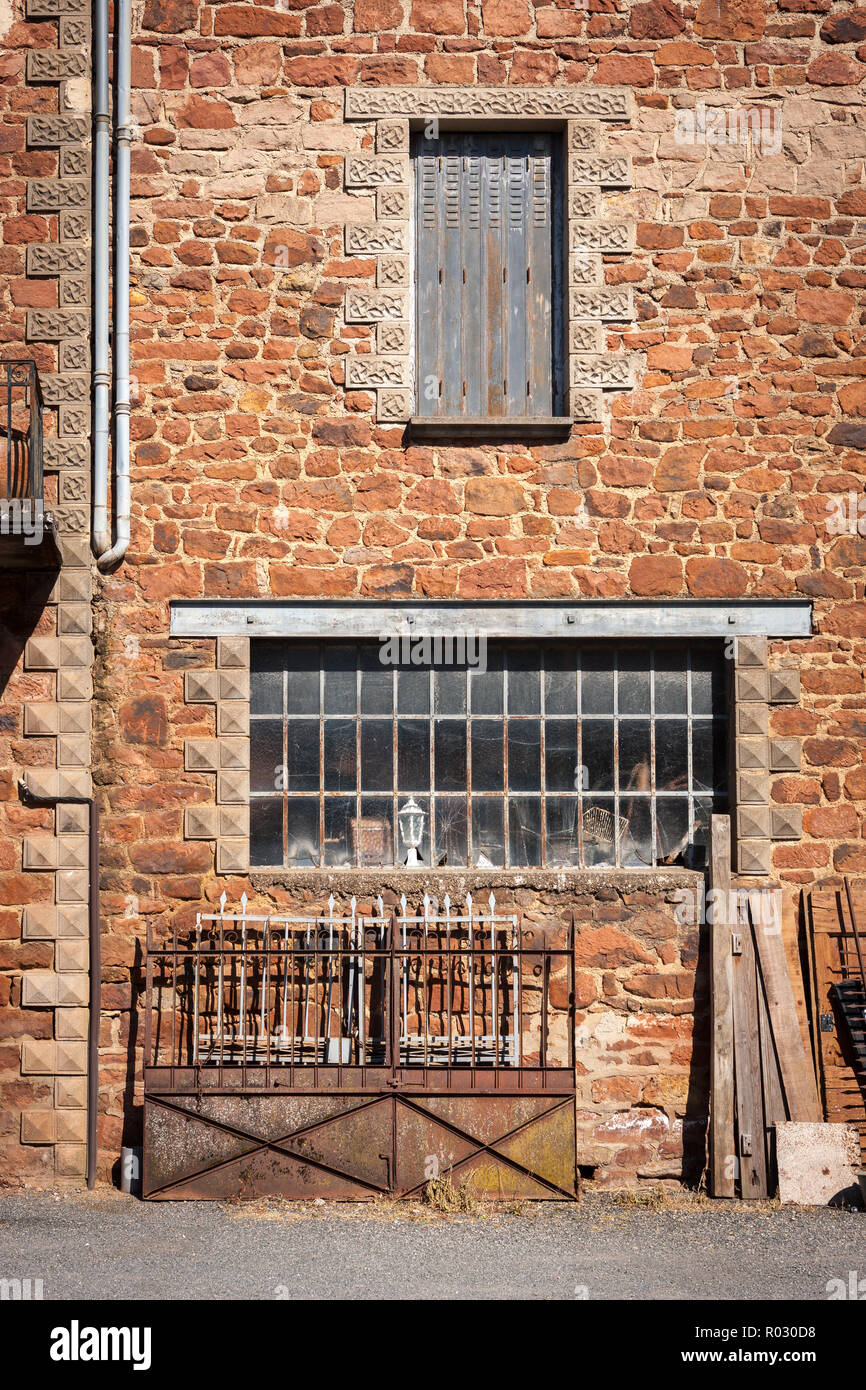 Old red stone building with cobwebs in the window and rusty metal gates outside and wooden planks Stock Photo