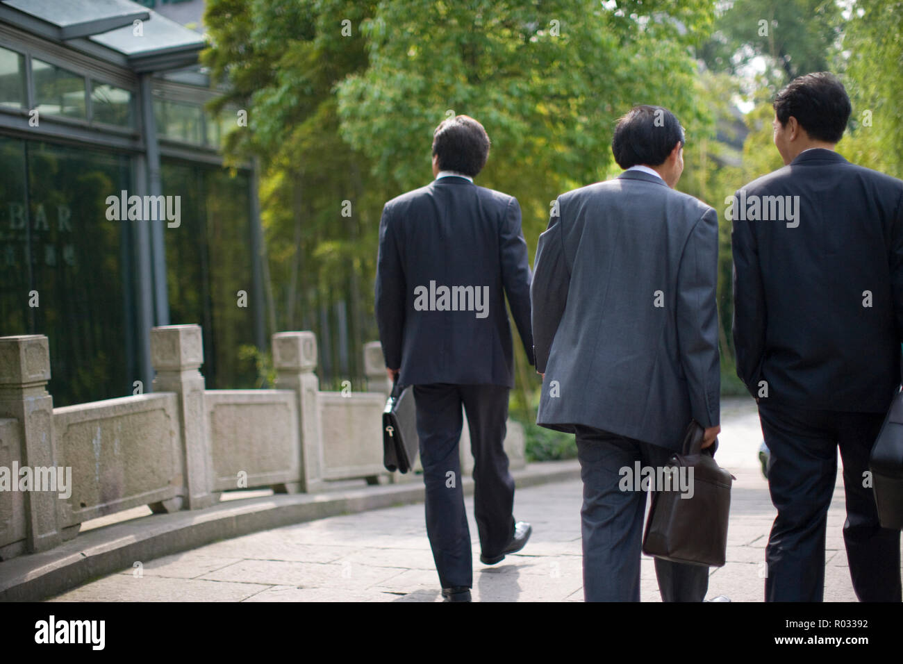 Three businessmen walking side by side over a paved bridge Stock Photo ...