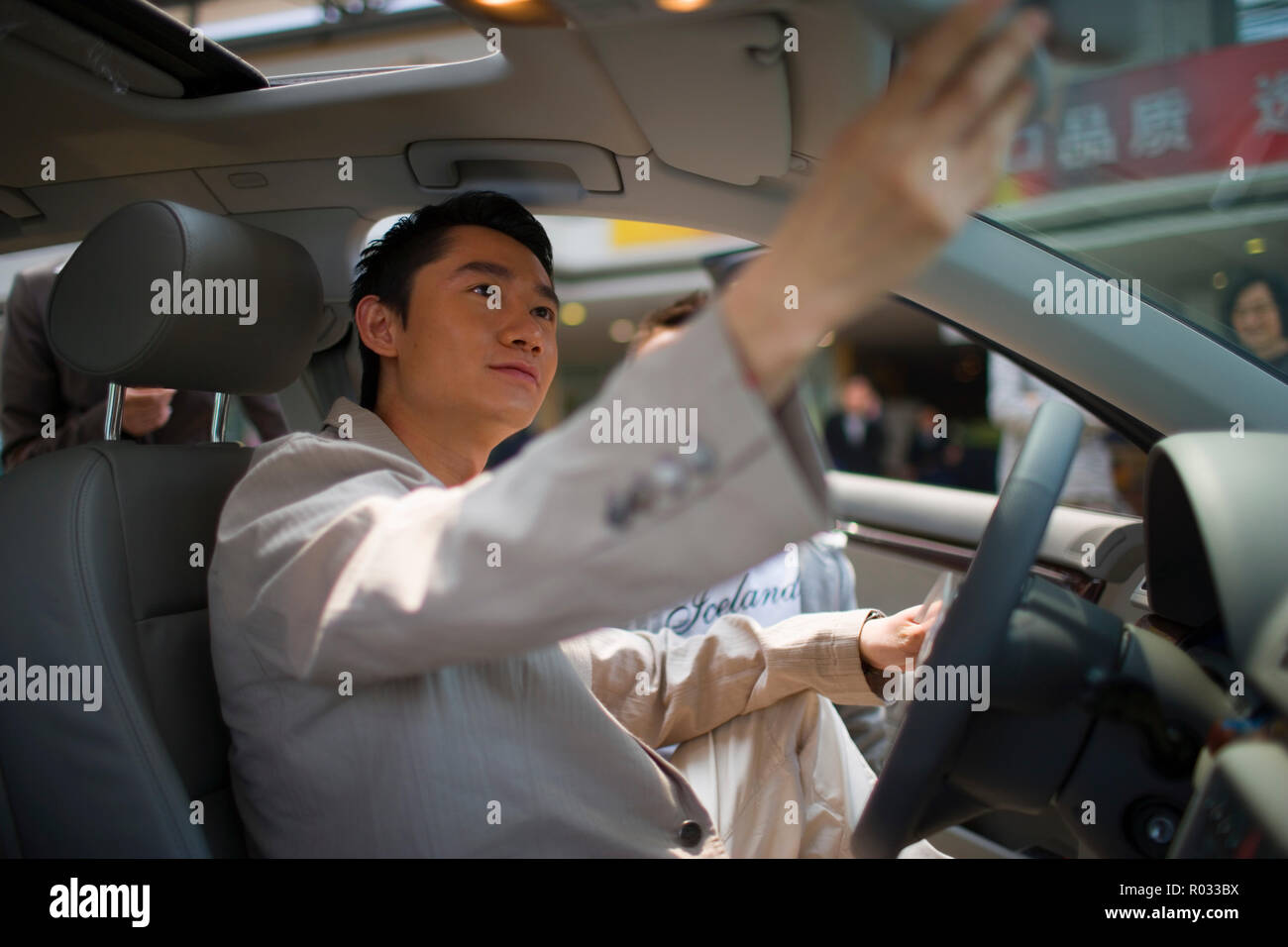 Young man sitting inside a car and adjusting the rearview mirror. Stock Photo
