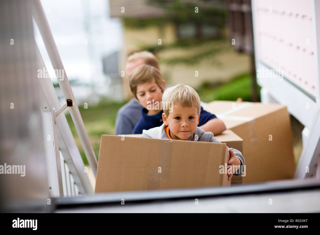 Young boy carrying boxes with his brother into a house. Stock Photo