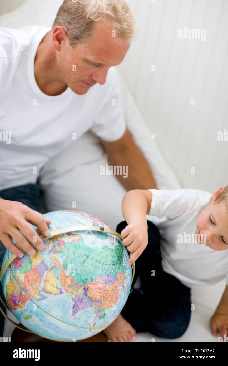 Mid-adult man sitting with his young son looking at a globe. Stock Photo