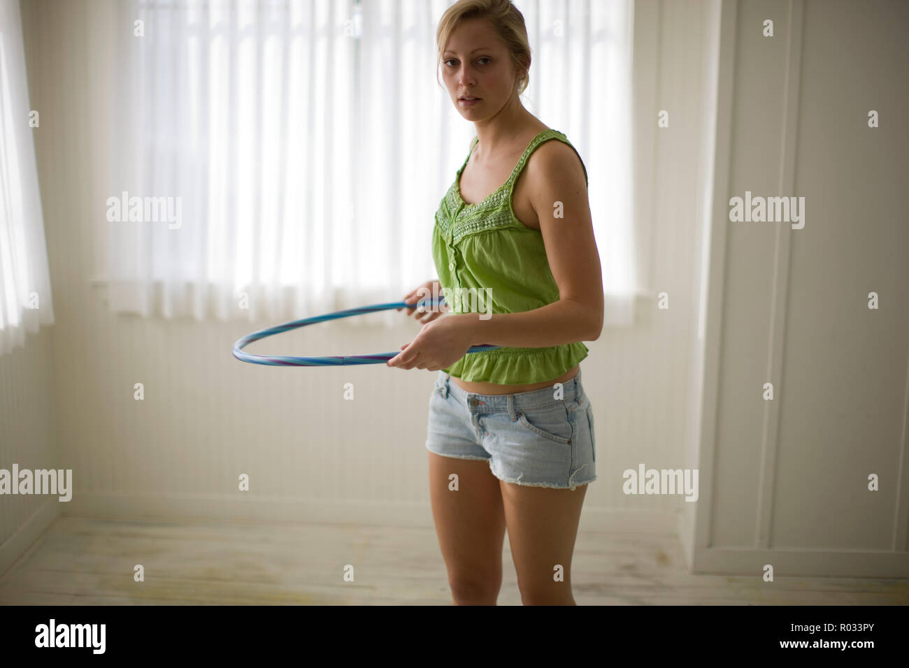 Portrait of a young adult woman with a hula-hoop in a room. Stock Photo