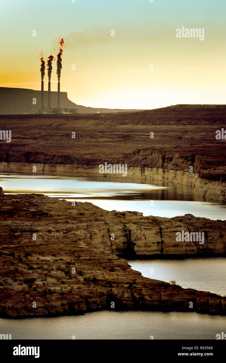 Factory chimneys pumping smoke into the air on a rocky landscape at sunrise. Stock Photo