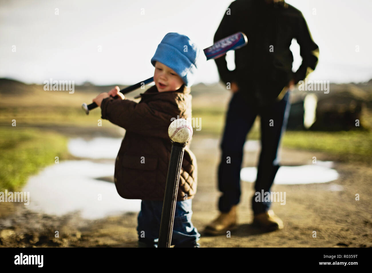 Little boy playing tee ball with his father watching in the background