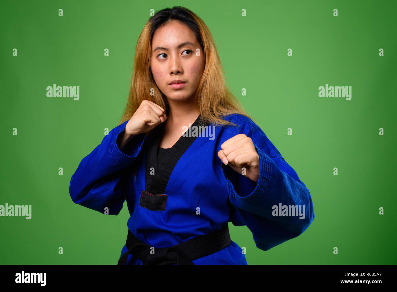 Young Asian woman wearing blue karate Gi against green backgroun Stock Photo