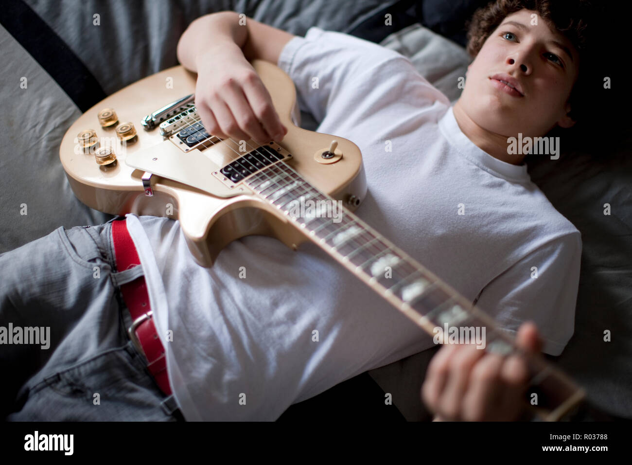 Boy lying on bed playing guitar. Stock Photo