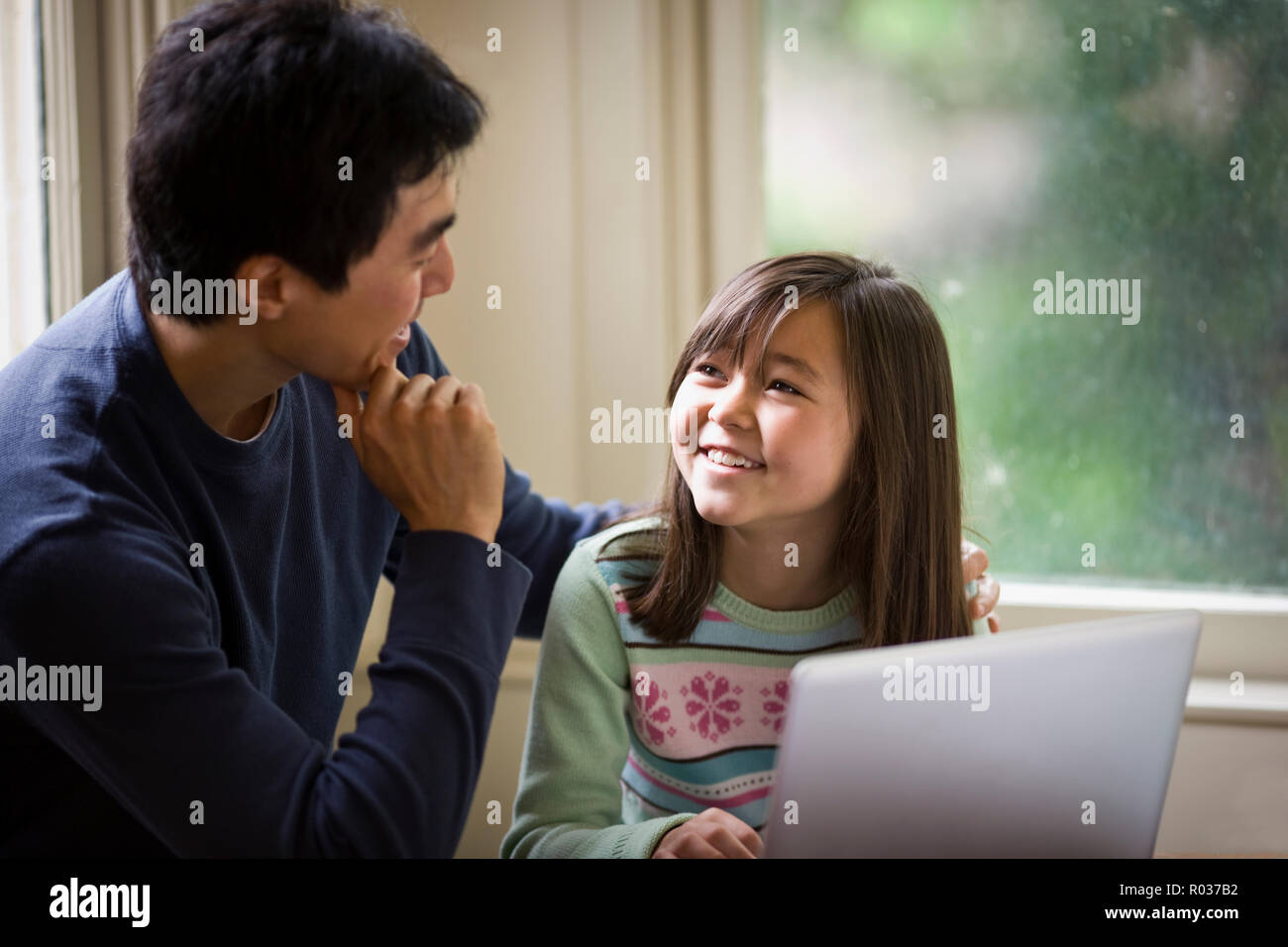 Father and daughter smile while working on a laptop together. Stock Photo