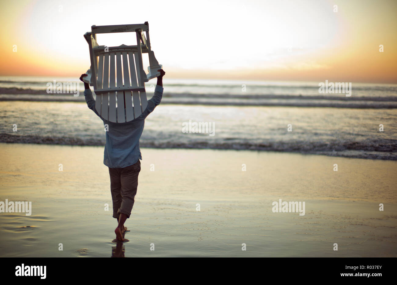 Middle aged man carrying a chair on a beach at sunset. Stock Photo