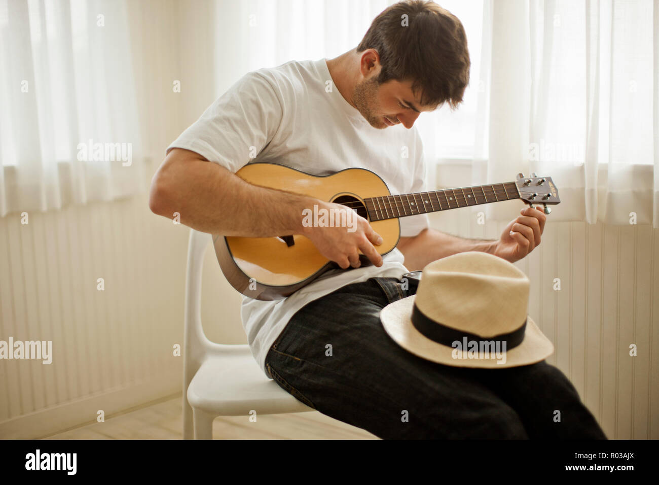 Young man playing a guitar while sitting on a chair Stock Photo - Alamy