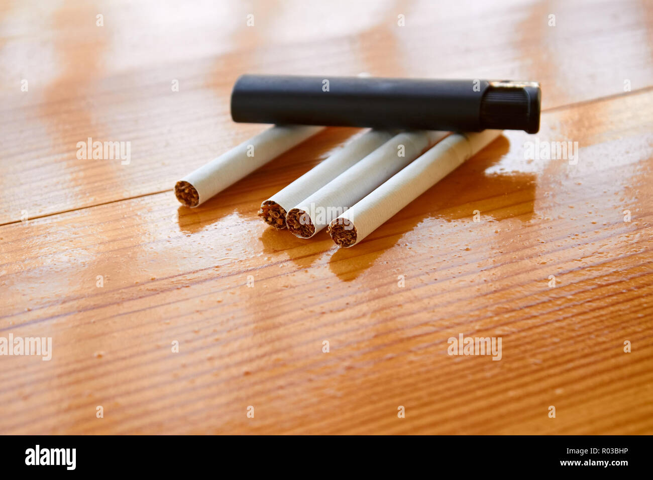 Four cigarettes and lighter on the lacquered wooden table Stock Photo