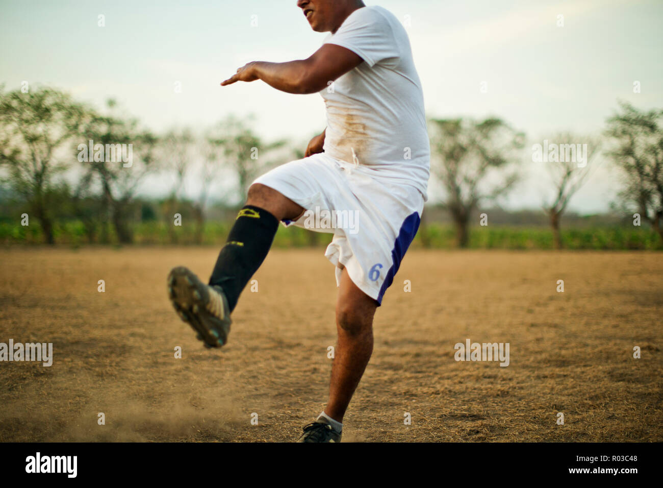 Young soccer player kicking his leg in the air while playing on a dusty soccer field. Stock Photo