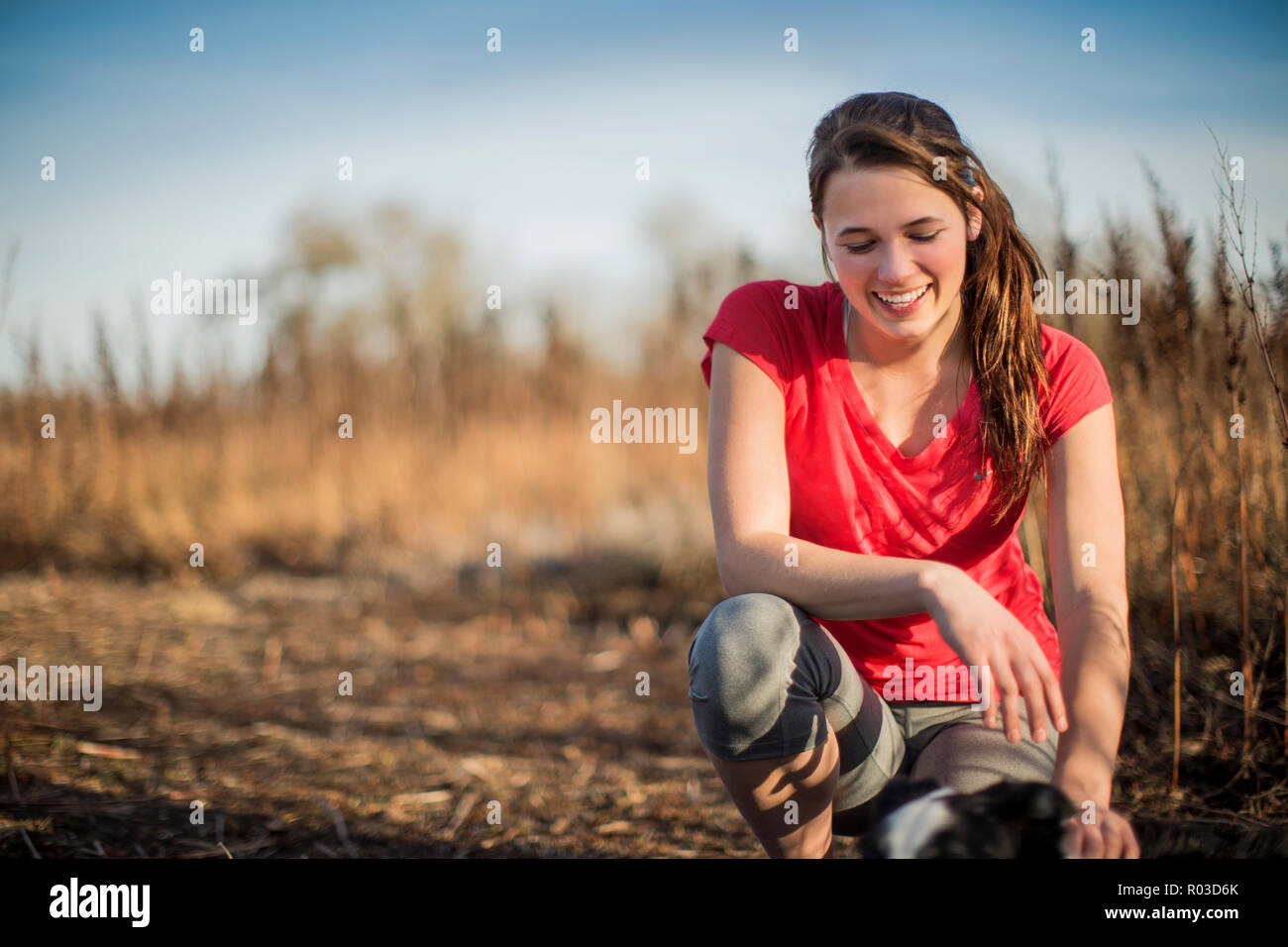 Smiling young woman takes a break from her countryside run in the late afternoon sunlight. Stock Photo