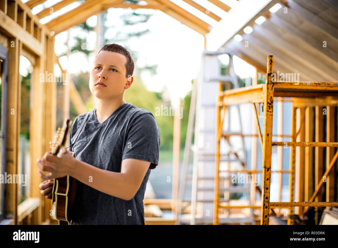Contented teenage boy playing a mandolin at a construction site. Stock Photo